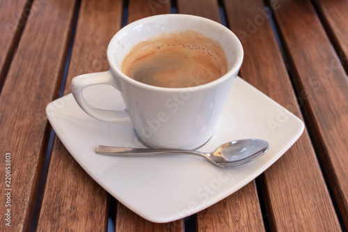 White cup of coffee with square sauser and spoon on a wooden table.