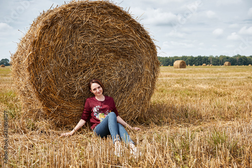 young girl having fun in the field, sits in a haystack and relaxing