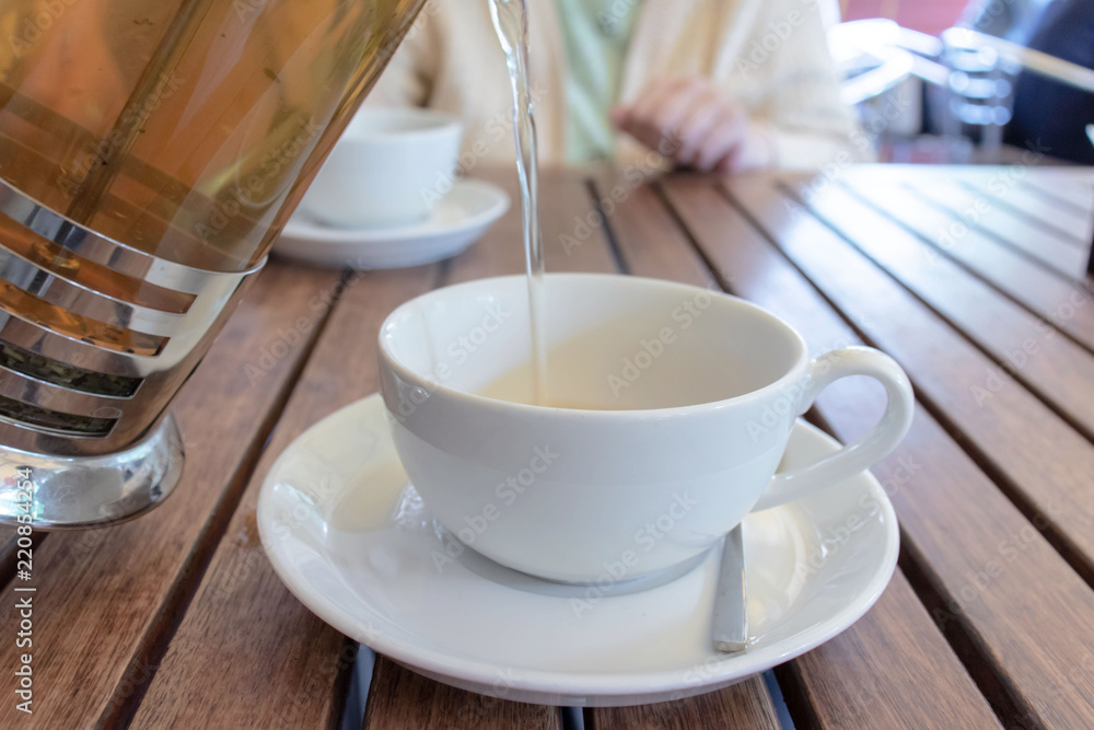 Two teacups and French press on the table, blurred woman behind. Pouring tea concept. Two teacups and French press on the table, blurred woman behind. Pouring tea concept.