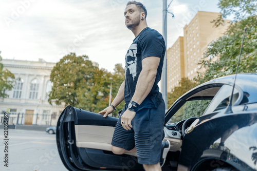 Close up of young attractive man getting out of the black car. Side view. © Akaberka
