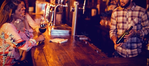 Canvas Print Bartender showing wine bottle to women at counter