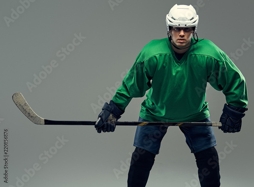 Portrait of a professional hockey player wearing full gear and a hockey stick on a gray background.