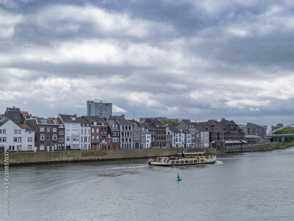 View to the Meuse River with a ship and beautiful old buildings against a moody overcast sky in Maastricht, Netherlands