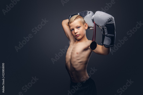 Canvas Print Young shirtless boy boxer in boxing gloves holds a golden medal posing in a studio