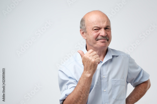 Senior attractive man frowning face as he is eating something sour and showing thumb up. He try to pretend that he approve your choice but emotion on his face is very negative