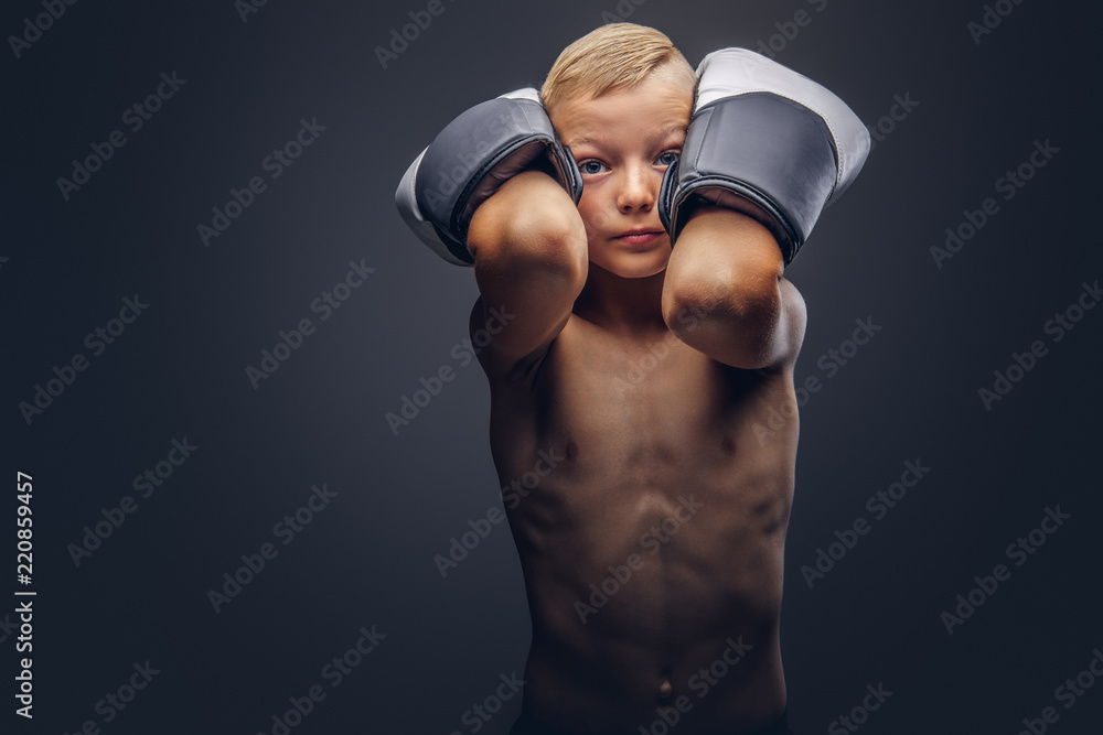 Shirtless boy boxer with blonde hair wearing boxing gloves workout in a studio.