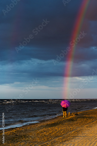 Rainbow above sea and woman on sandy beach of the Baltic Sea during sunset, J...