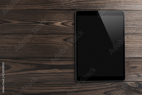 Black tablet computer on wooden dark background with space for text, flat lay
