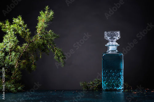 Blue gin in crystal decanter and juniper branch with berries.