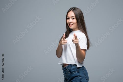 Happy young Asian woman pointing her finger at camera on gray background