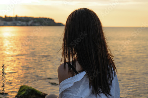 silhouette of a long-haired girl in a white shirt on a background of a stunning sunset, dawn on the sea © Viktoria