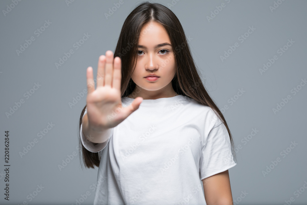 Portrait of a serious young asian woman standing with outstretched hand showing stop gesture isolated over gray background Portrait of a serious young asian woman standing with outstretched hand showing stop gesture isolated over gray background