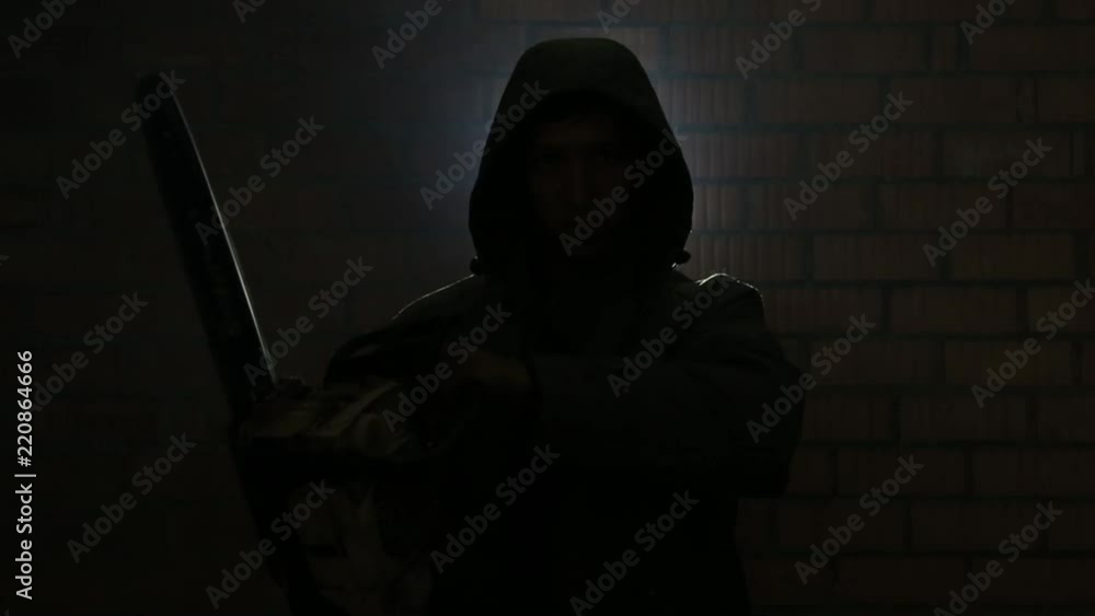 Maniac in the hood with a chainsaw near the brick wall waiting for the victim Maniac in the hood with a chainsaw near the brick wall waiting for the victim