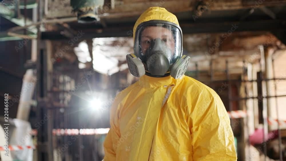 Portrait of young Caucasian guy wearing respirator mask and yellow hazmat suit. Slavic scientist with brown eyes looking at camera. Indoors. Radiation. Portrait of young Caucasian guy wearing respirator mask and yellow hazmat suit. Slavic scientist with brown eyes looking at camera. Indoors. Radiation.