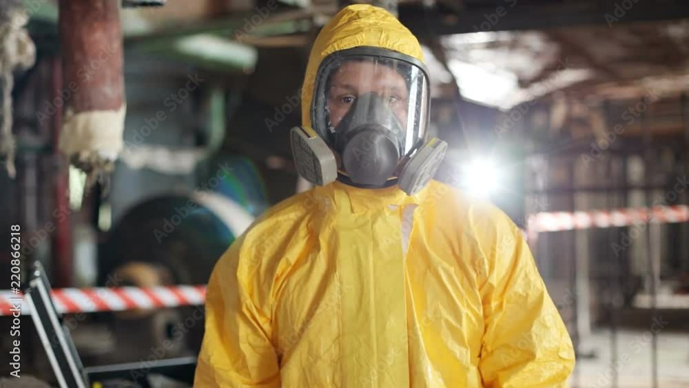 Guy in gas mask looking directly at camera. Young man wearing yellow hazmat outfit and red rubber gloves at work in old building. Portrait. Close-up. Guy in gas mask looking directly at camera. Young man wearing yellow hazmat outfit and red rubber gloves at work in old building. Portrait. Close-up.