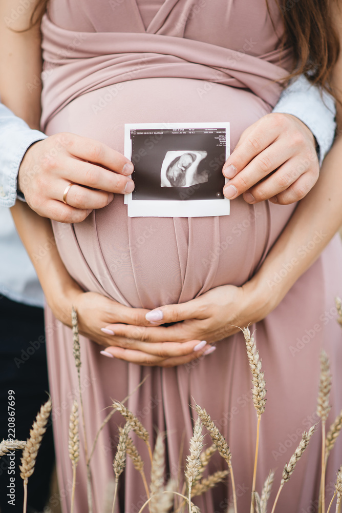 Close-up of unrecognizable pregnant woman with ultrasound picture in hand