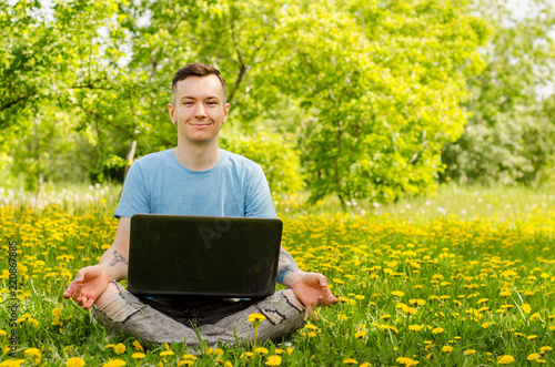 Young gyu freelincer at work on a laptop on a green grass and trees background.