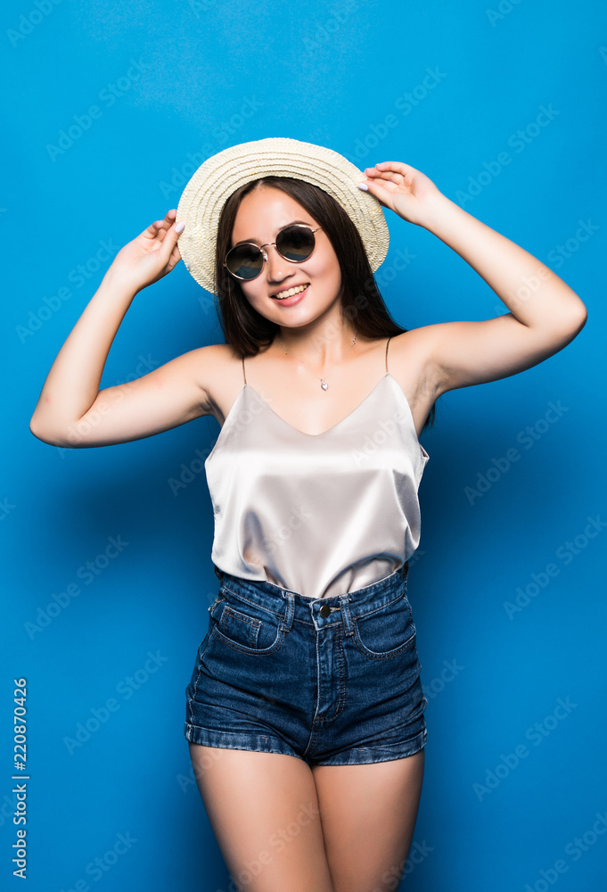 Portrait of stylish cute smiling asian girl wears straw hat and trendy glasses posing on blue background