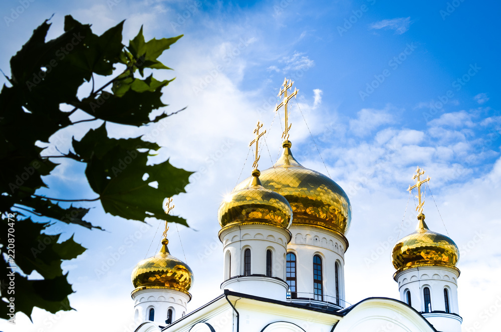 White orthodox church with gold domes (cupolas) against the blue sky