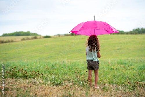 une enfant aux cheveux long et bouclés se met à l'abris sous un parapluie rose