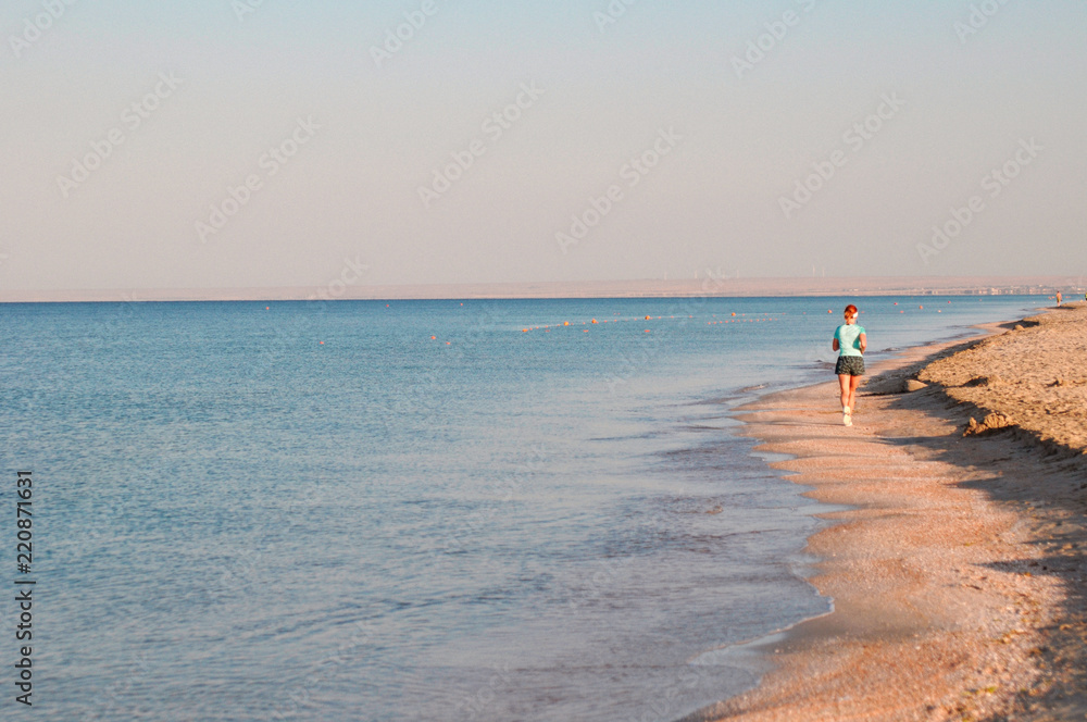 A girl on the beach makes a morning jog along the sea. Sport