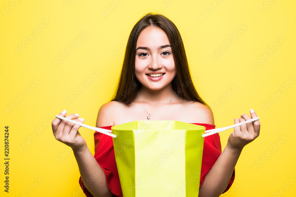 Portrait of a happy pretty asian woman looking inside shopping bag isolated over yellow background Portrait of a happy pretty asian woman looking inside shopping bag isolated over yellow background