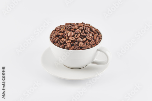 White coffee cup filled with whole coffee beans on a saucer  isolated on white background. View slightly from above.