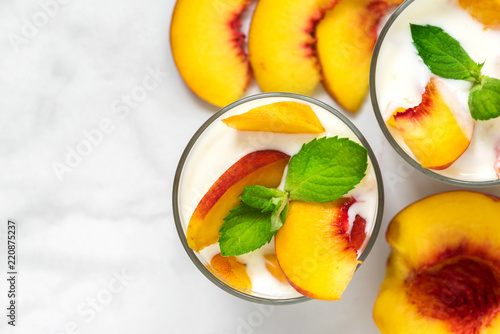 Fototapeta Naklejka Na Ścianę i Meble -  two glasses of healthy fruit yogurt with fresh peaches and mint on white marble table. healthy breakfast. top view