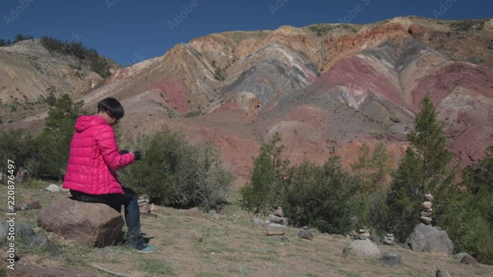 A woman is taking pictures of beautiful mountains sitting on a rock. A woman is taking pictures of beautiful mountains sitting on a rock.