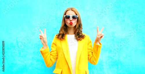 Fashion portrait woman sends an air kiss in a yellow coat posing on a blue background