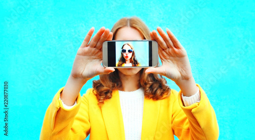 Obraz na plátně woman takes picture self portrait on smartphone on colorful blue background