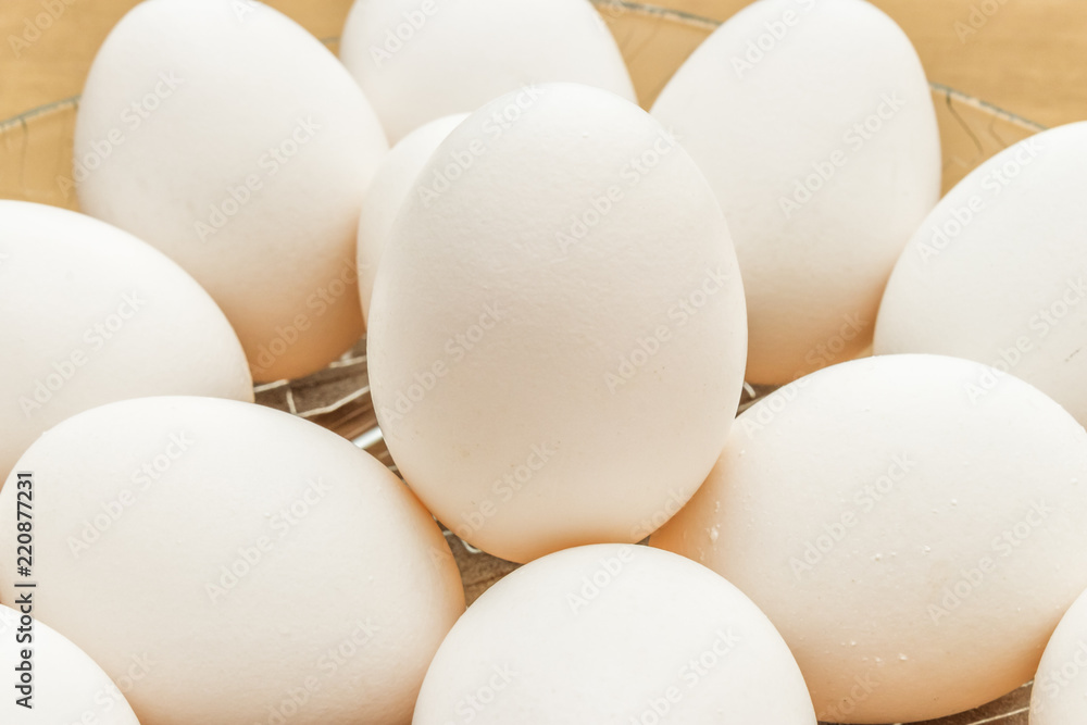 close up on white eggs arranged in glass basket on wooden table close up on white eggs arranged in glass basket on wooden table