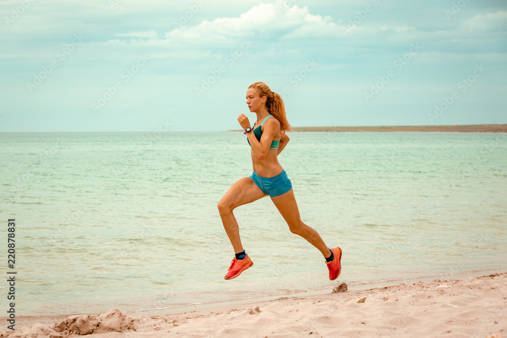 Beautiful sportive woman running along beautiful sandy beach, healthy lifestyle, enjoying active summer vacation near the sea Beautiful sportive woman running along beautiful sandy beach, healthy lifestyle, enjoying active summer vacation near the sea