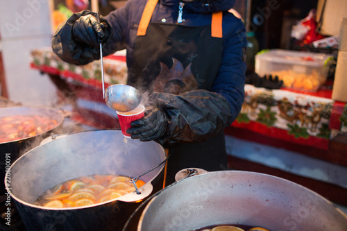 Hot gluhwein or mulled wine in a cauldron at fair, local treat, warm and spicy. A hot wholesome traditional citrus drink on fair. Vitamins in the winter festival. Pour the drink into a glass or a cup.