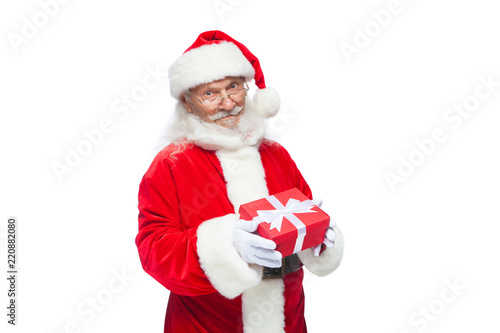Christmas. Smiling Santa Claus in white gloves is holding a gift red box with a bow. Pointing at the gift. Isolated on white background.