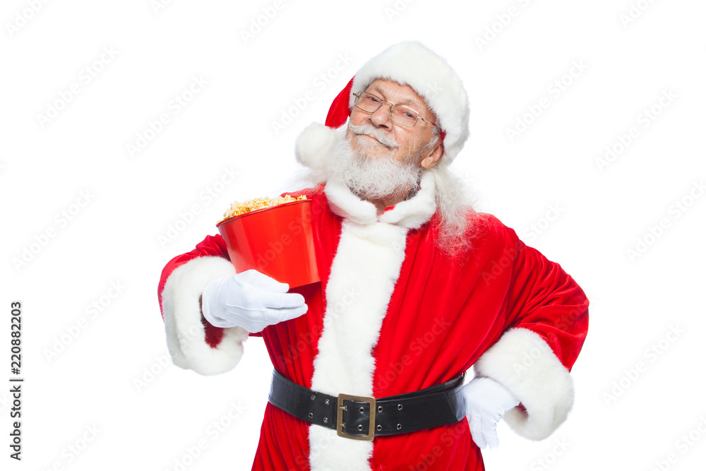 Christmas. Smiling, kind Santa Claus in white gloves holds a red bucket with popcorn with one hand, and puts the other hand on his belt. The concept of visiting the cinema, watching a movie with Christmas. Smiling, kind Santa Claus in white gloves holds a red bucket with popcorn with one hand, and puts the other hand on his belt. The concept of visiting the cinema, watching a movie with
