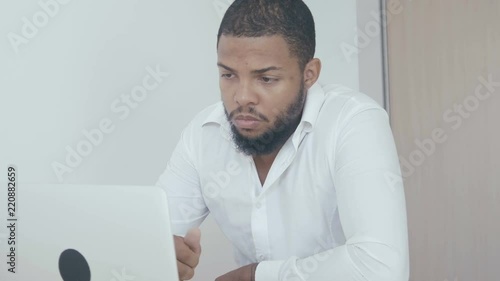 Serious black man working use computer looking in monitor screen at office. African american businessman worling at laptop. photo