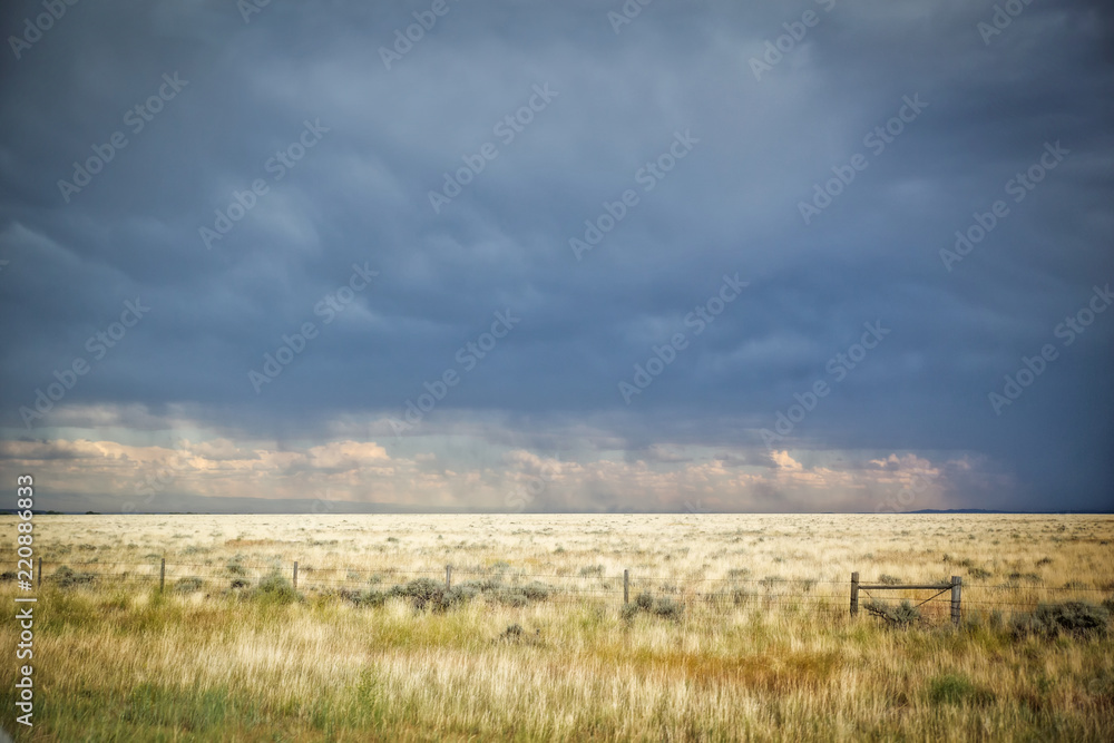 Fenced pasture land under a stormy blue sky in a afternoon summertime landscape in rural montana