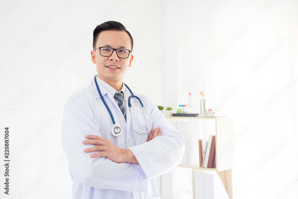 Young asian male doctor standing in hospital office and smiles at camera