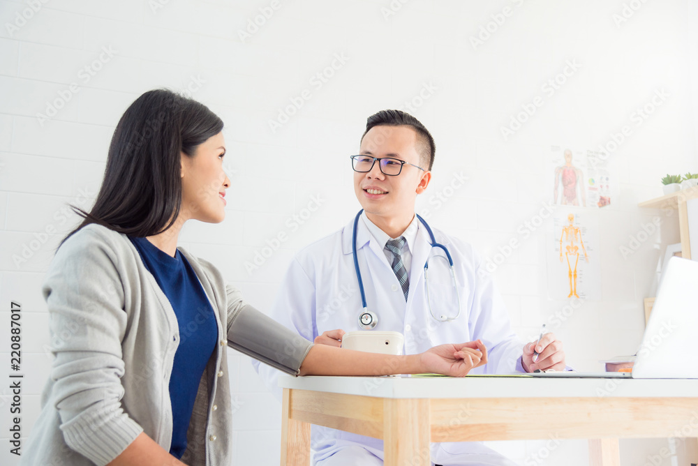 Fototapeta premium Young asian male doctor checking female patient blood pressure at clinic