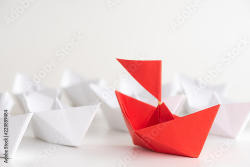 Leadership concept. red paper ship lead among white. One leader ship leads other ships.
