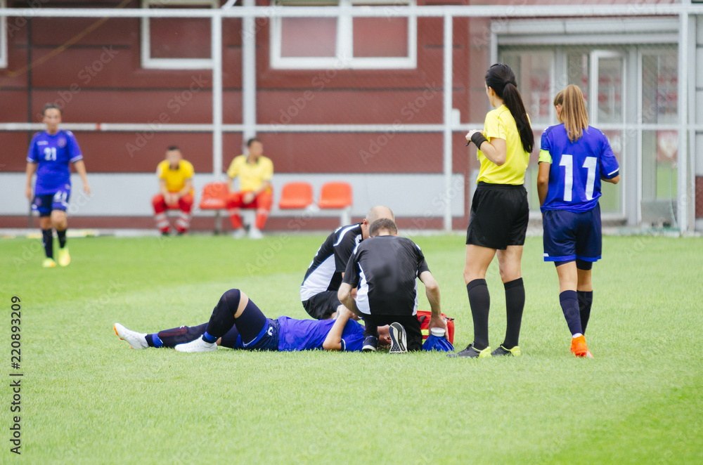 Fototapeta premium Women football player lying injured on ground, while medic team helping her.
