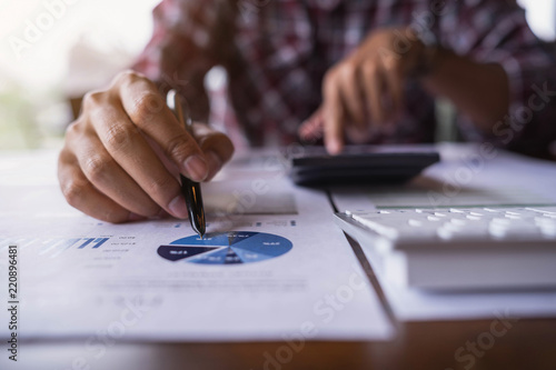 Close up of businessman point the pen on graph of the business data financial report and using calculator to calculate number. Business financial analysis and strategy concept.