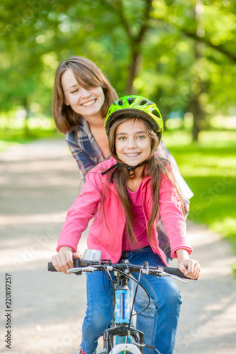 mom teaches her daughter to ride a bicycle in the park