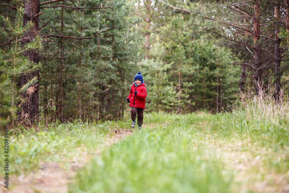cheerful boy in a red jacket running in the forest