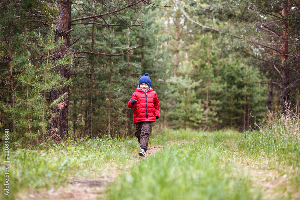 cheerful five-year-old boy in a warm cap and down jacket running through the woods cheerful five-year-old boy in a warm cap and down jacket running through the woods