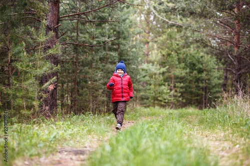 cheerful five-year-old boy in a warm cap and down jacket running through the woods