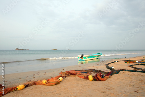 фотографія Fishing boat beached next to fishing nets with floats drying on Nilaveli beach i