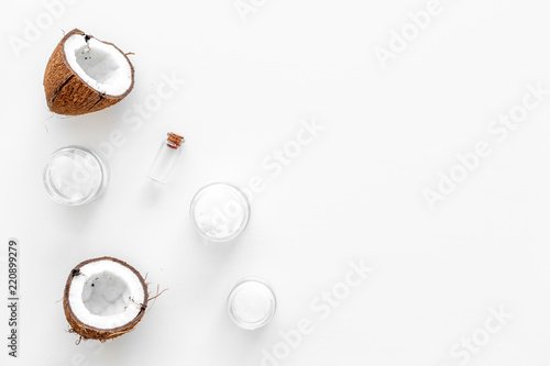 Coconut oil cosmetics for skin and hair care. Oil in small bottle, cream jar, halfs of coconut with shelf on white background top view copy space