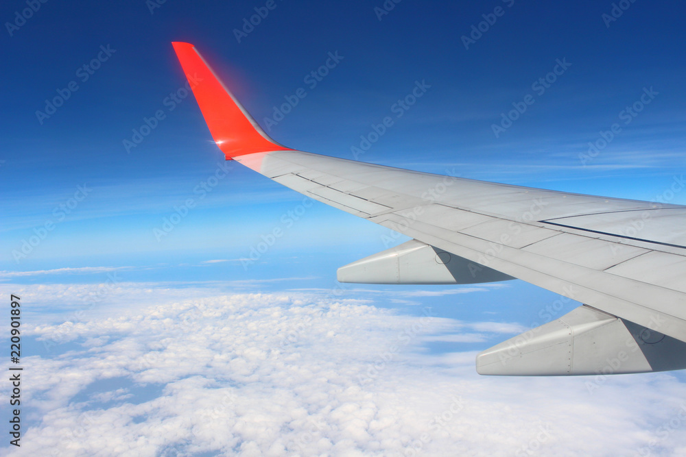 Wing of an airplane flying above the cloud looks from the window of the plane